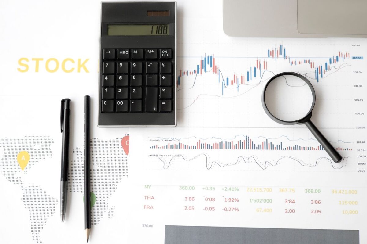 our-experience Flat lay of stock market analysis tools including calculator, graphs, and magnifying glass.